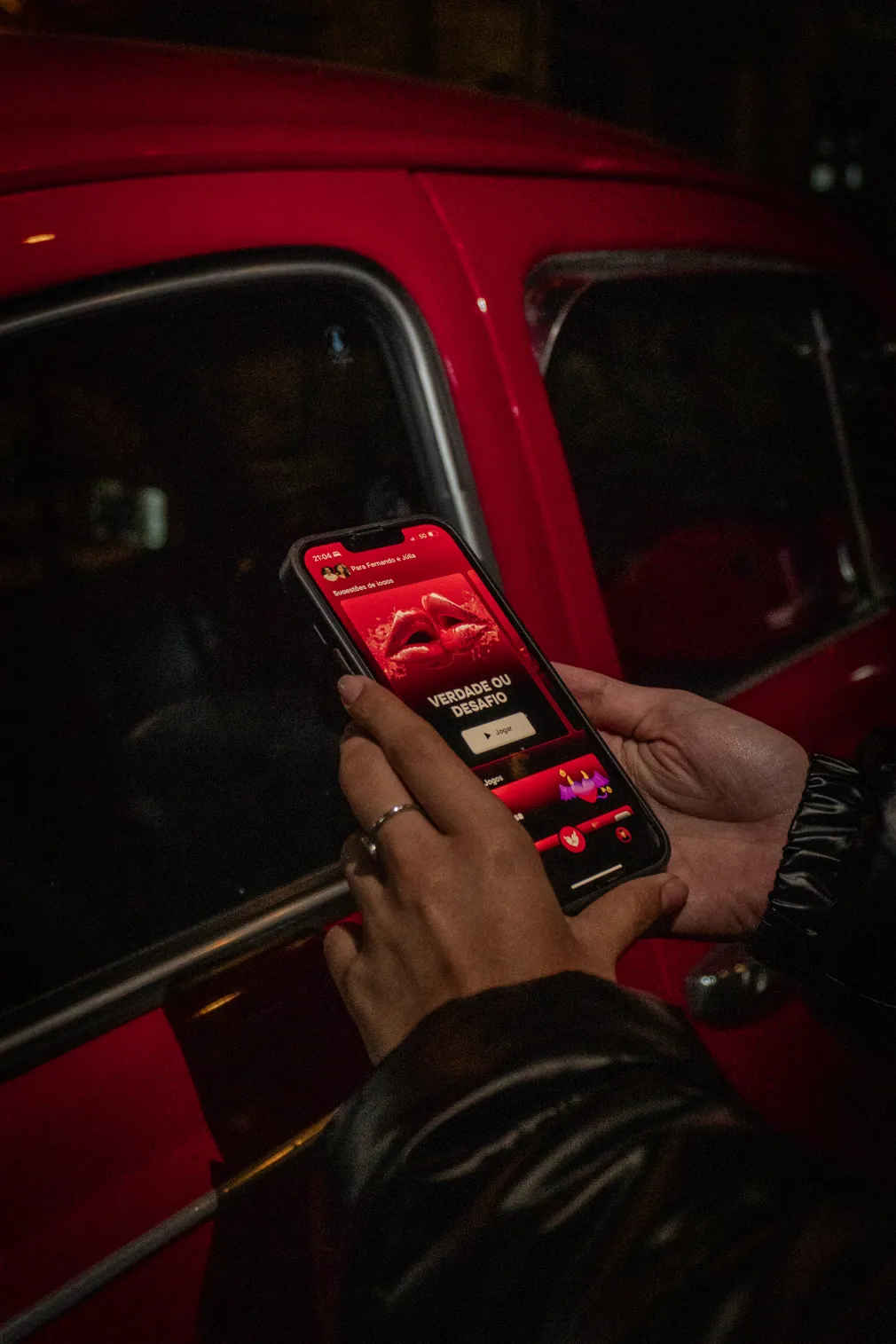 A hand holding a phone with Heat open, next to a red car at night